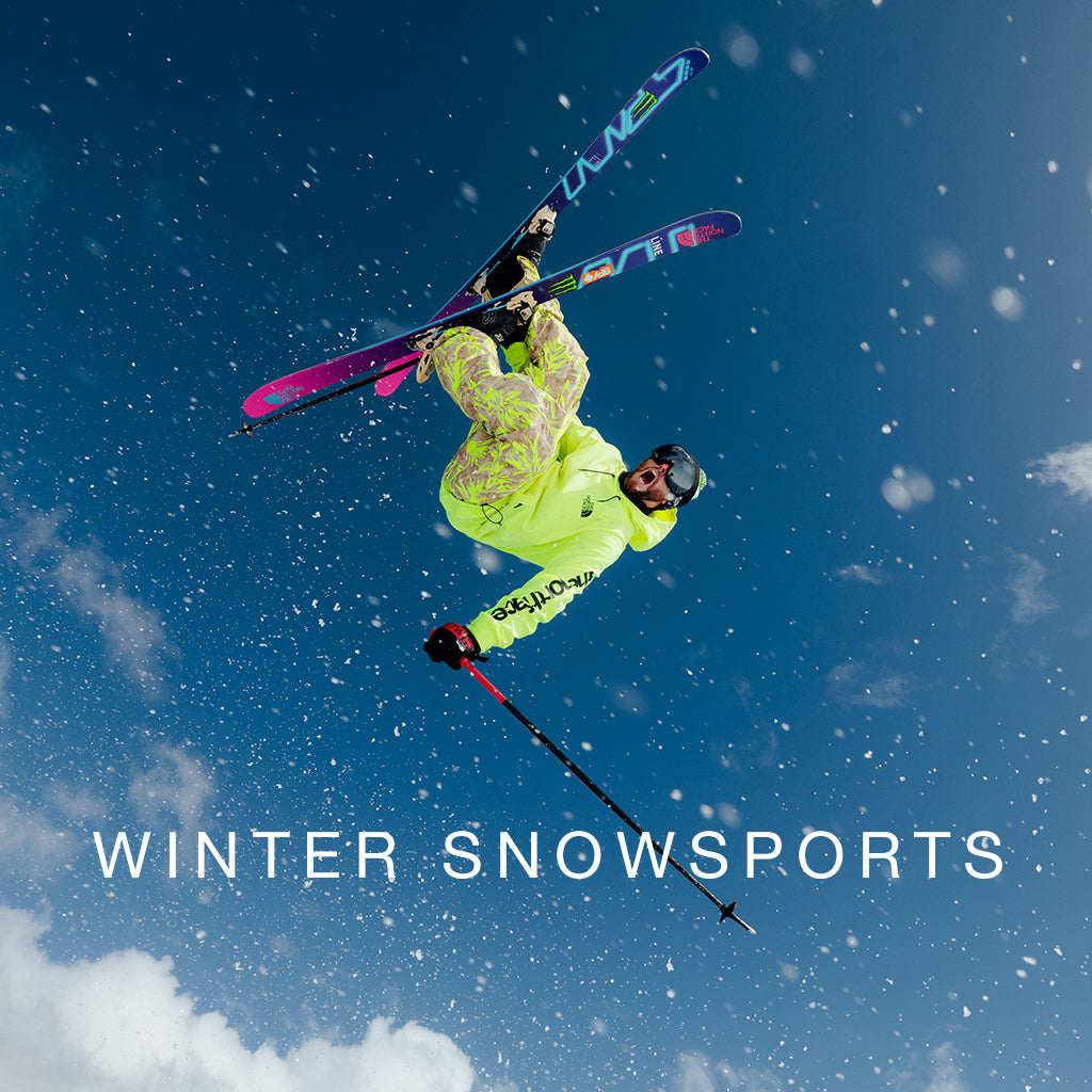SHOP WINTER SNOWSPORTS - Skier flying upside down through the blue sky with his skis crossed.